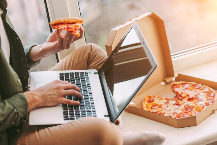 Persona trabajando en su laptop comiendo pizza a domicilio