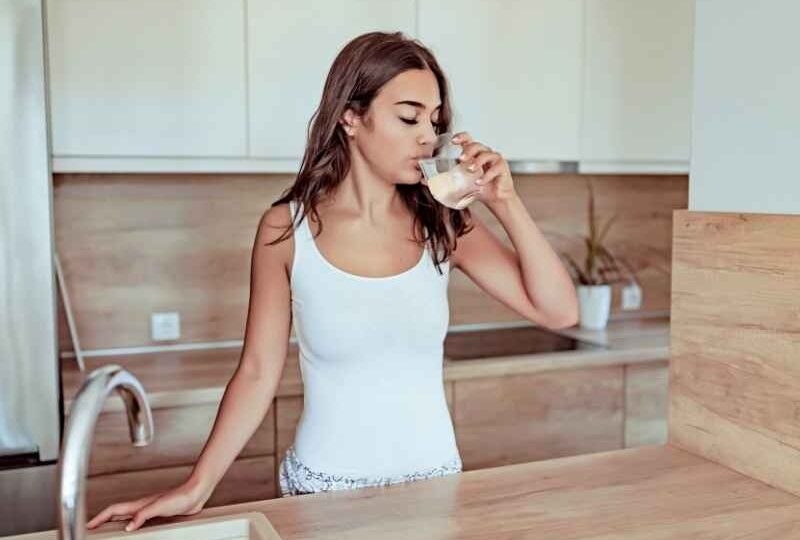mujer bebiendo agua en casa como hábito para prevenir olor fuerte en la orina
