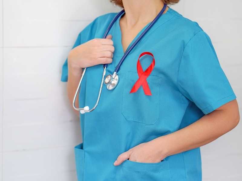 Profesional de la salud con bata azul y listón rojo en el pecho, representando la importancia de la prevención y detección del VIH y su carga viral