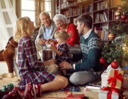 Familia de varias generaciones convive junto al árbol de Navidad con los abuelos, representando reuniones invernales seguras y llenas de cariño.
